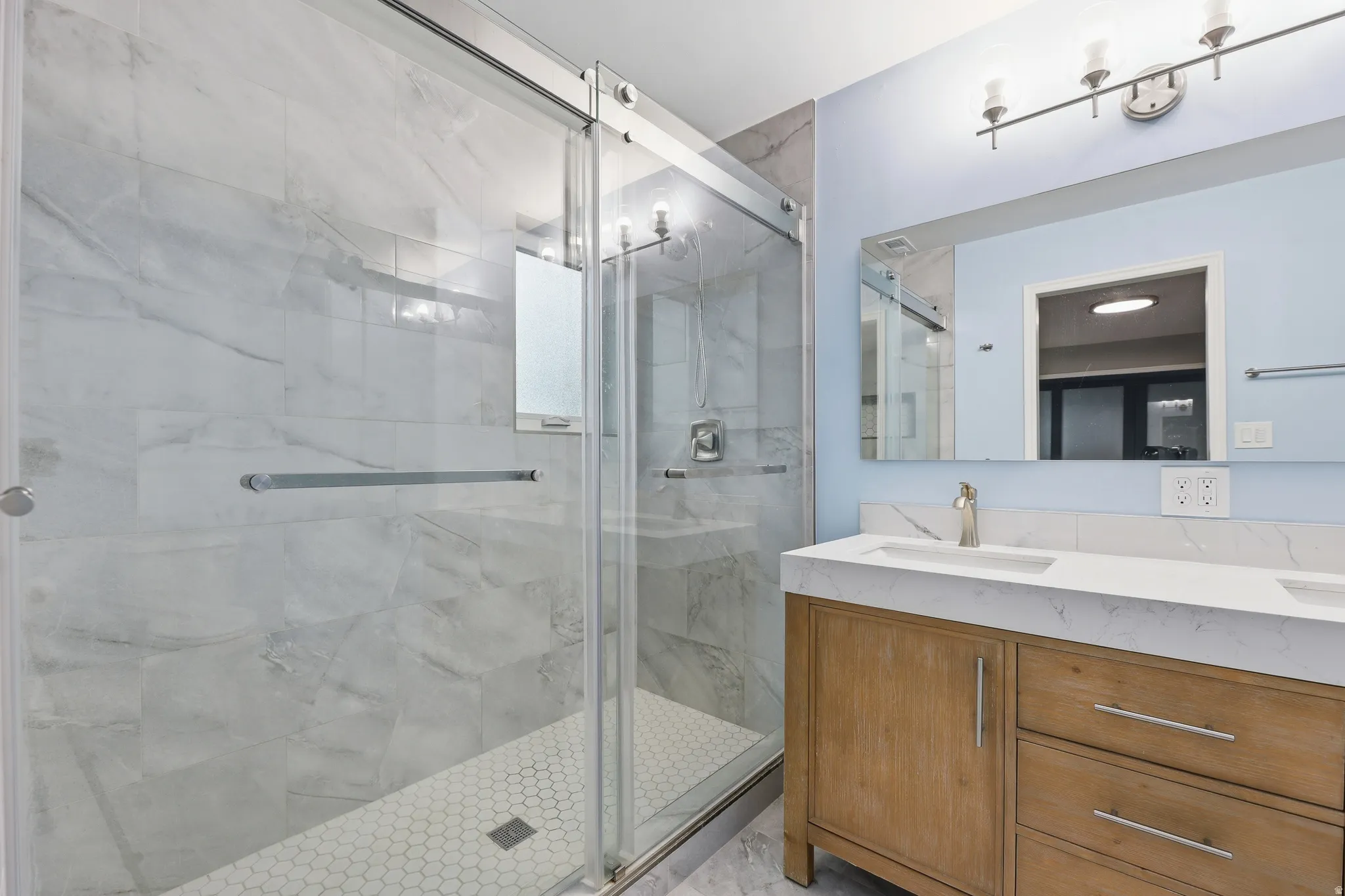 Walk-in shower with full-height marble-look tile surround and hex tile flooring