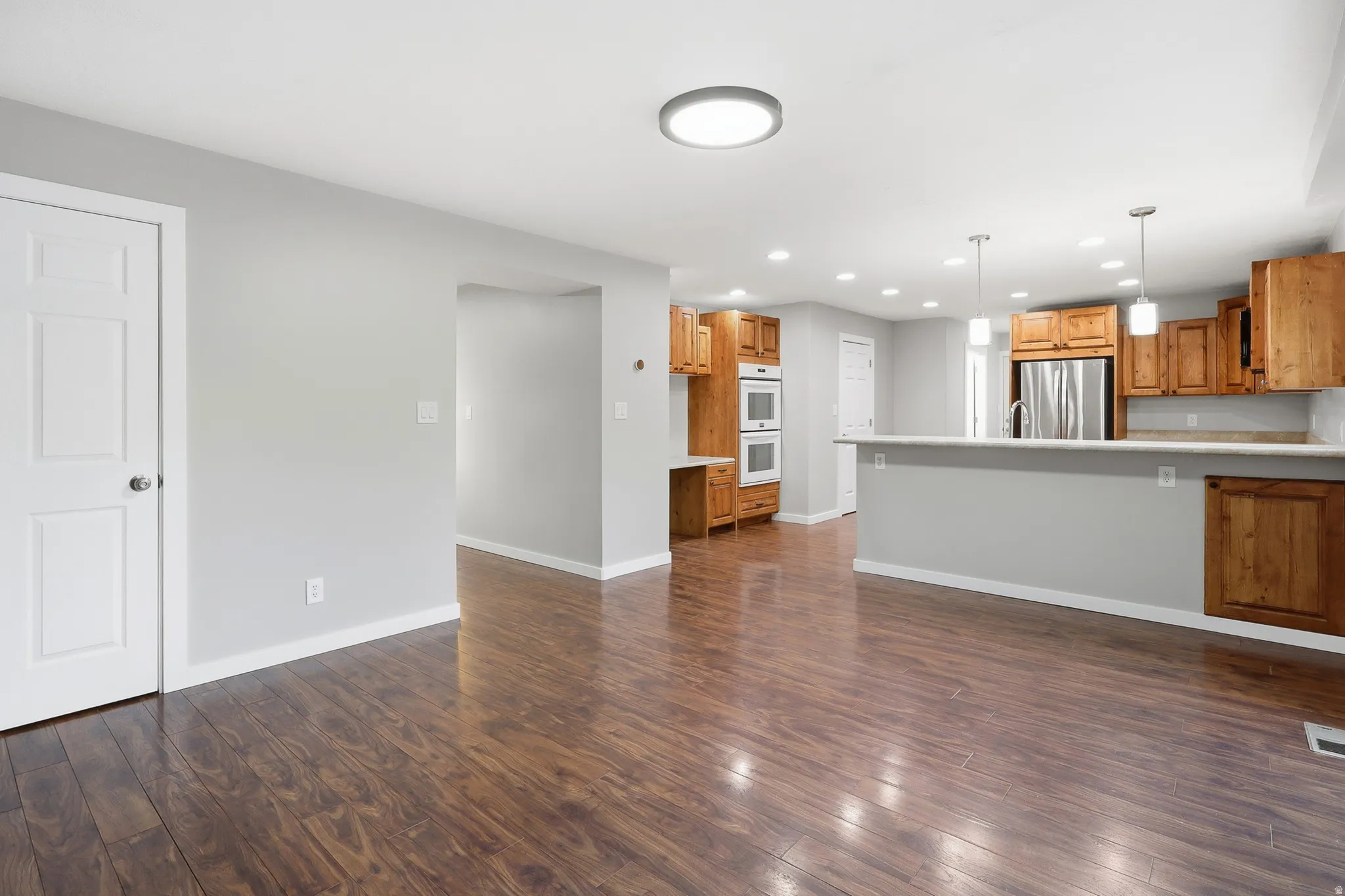 Wood-finish flooring, light gray walls, built-in double ovens, stainless steel refrigerator, and pendant lighting