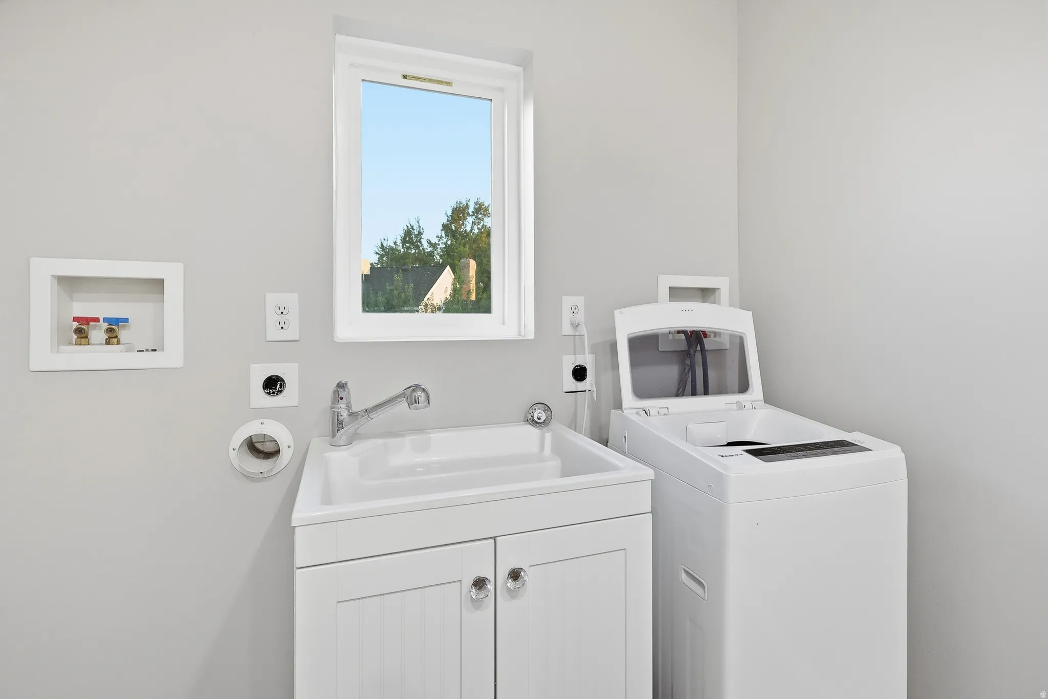 White utility sink with integrated faucet, white base cabinet with crystal knobs, and a white framed window
