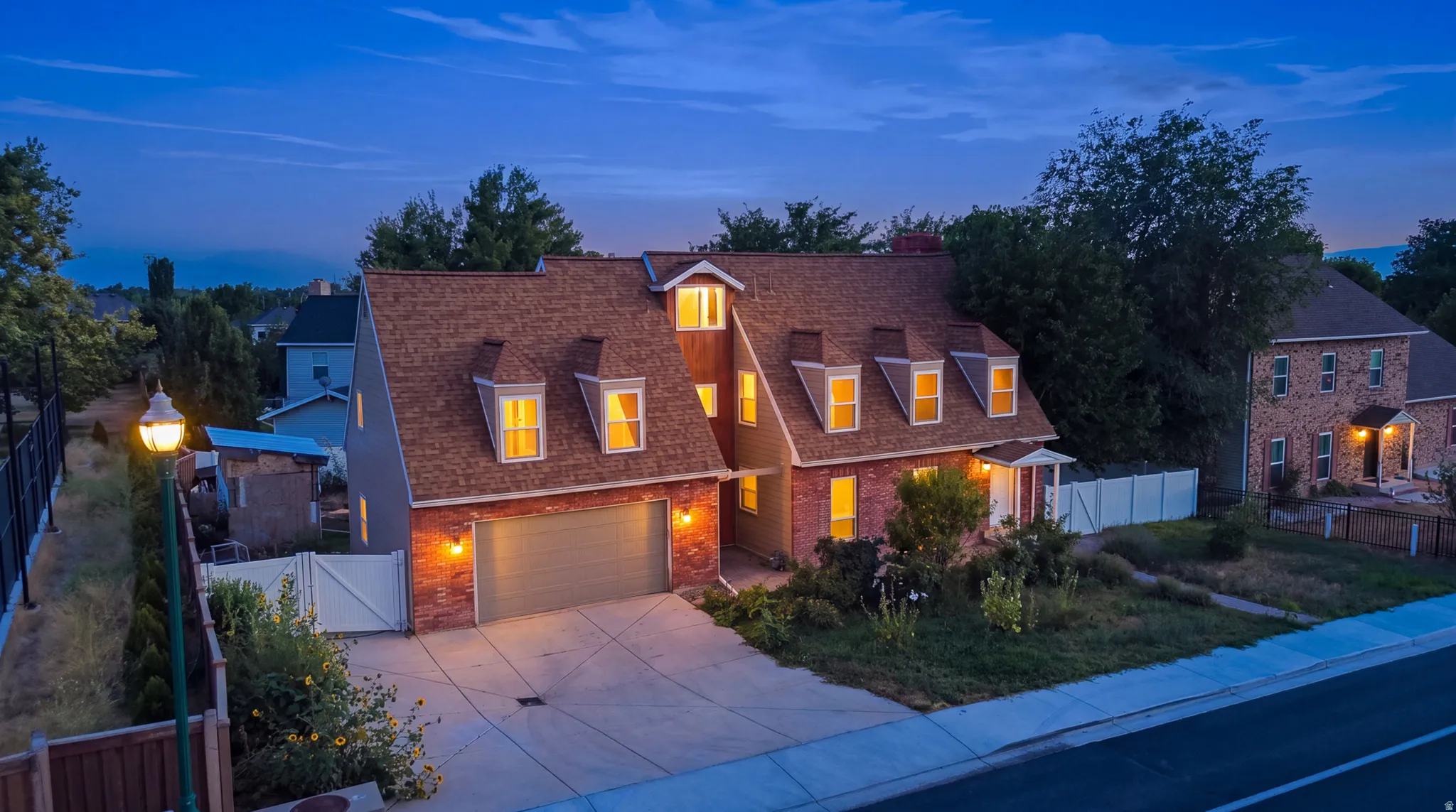 Brick exterior with dormer windows, attached garage, concrete driveway, and white fencing