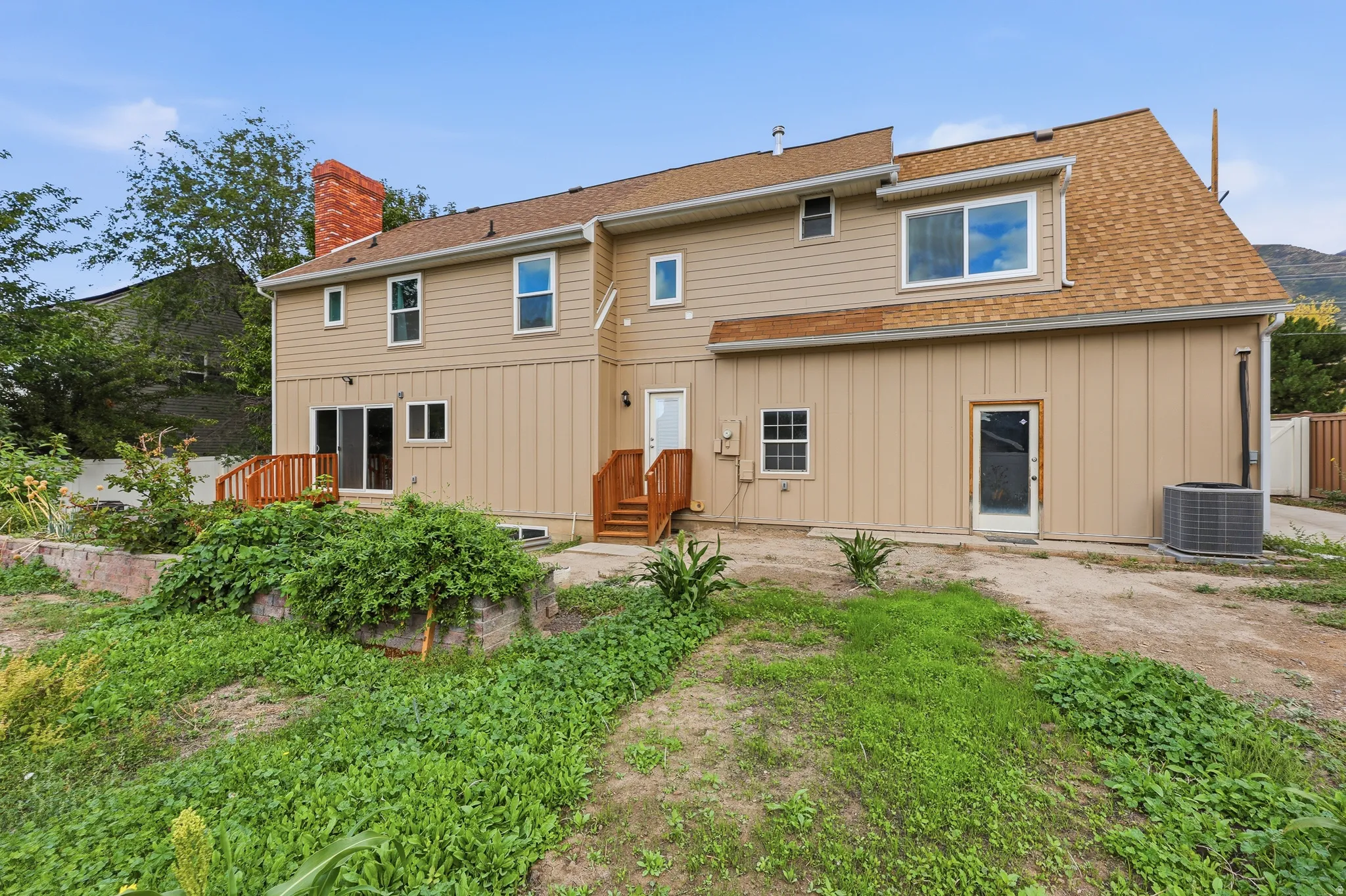 Rear elevation with tan siding, red brick chimney, and a wooden deck with railing