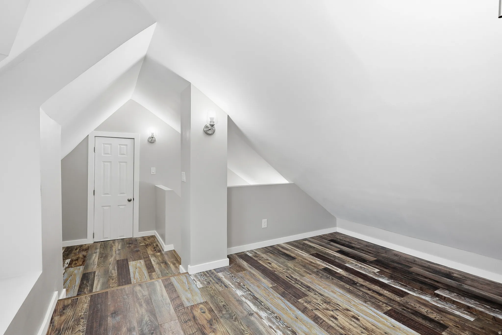 Sloped ceilings with recessed lighting, wood-finish flooring, interior door, and wall-mounted sconces