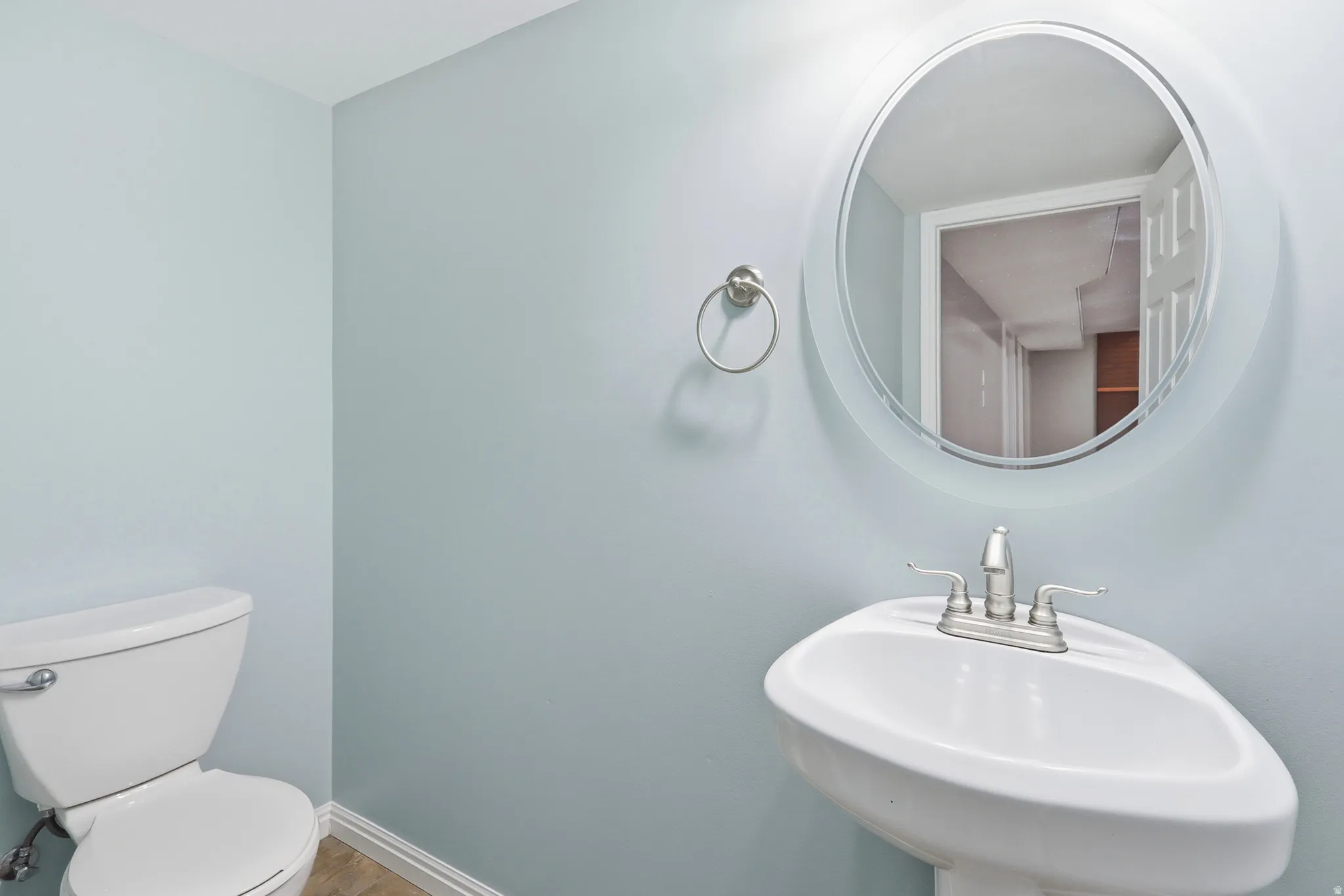White pedestal sink with a dual-handle faucet, circular wall mirror, and toilet