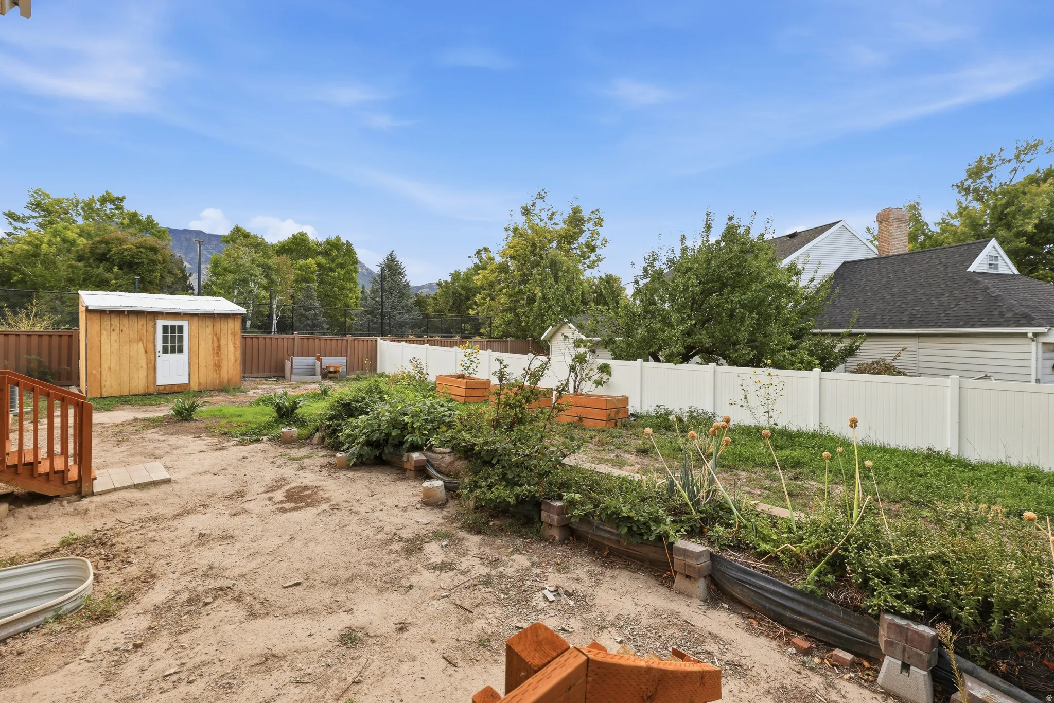 Fenced yard featuring a wooden shed, raised garden beds, and wood deck stairs