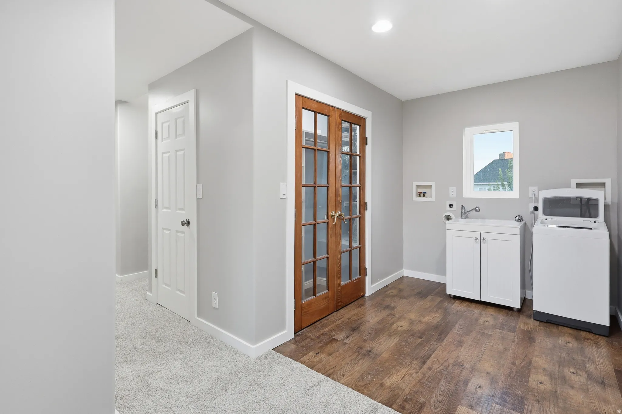 Laundry area featuring wood-finish flooring, a white utility sink cabinet, and a window