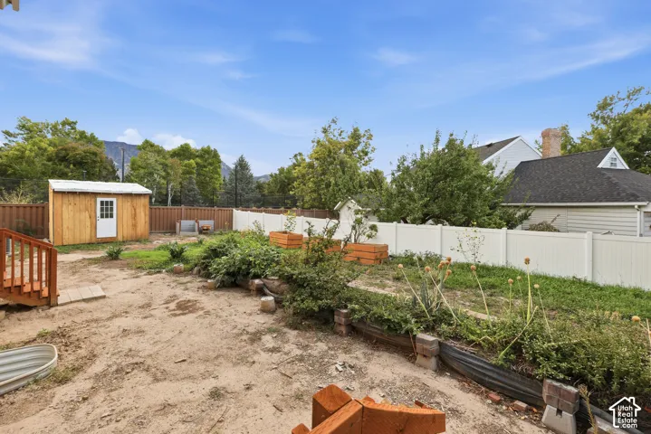 Fenced yard featuring a wooden shed, raised garden beds, and wood deck stairs