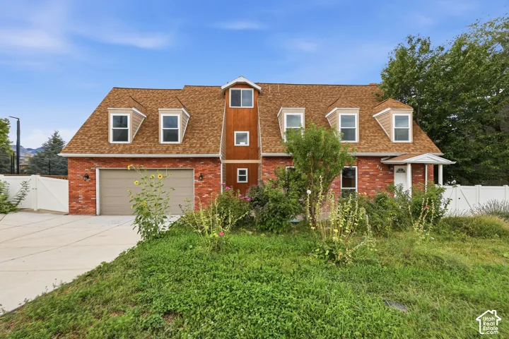 Brick exterior with a dormer roof, attached garage, and white perimeter fencing