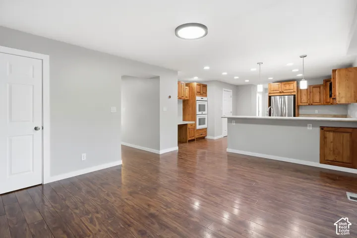 Wood-finish flooring, light gray walls, built-in double ovens, stainless steel refrigerator, and pendant lighting