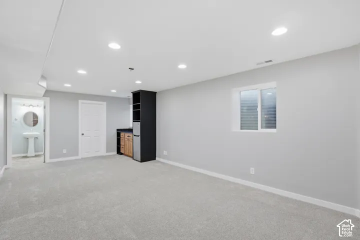 Recessed lighting, light gray carpet, and a built-in wet bar with wood-finish cabinetry