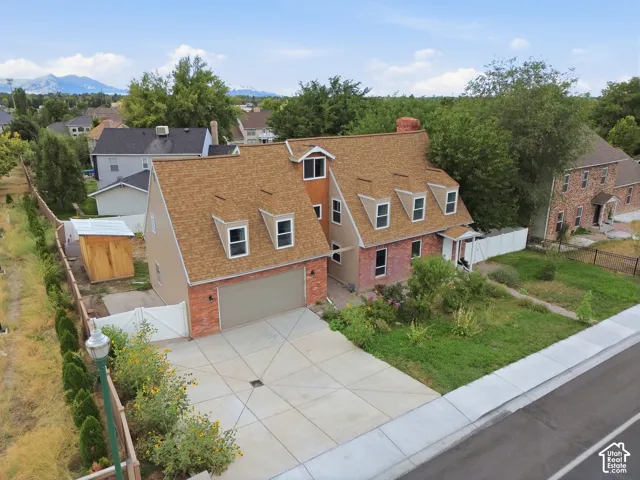 Brick and siding exterior, multi-dormer roofline, attached two-car garage, concrete driveway, and white picket fencing
