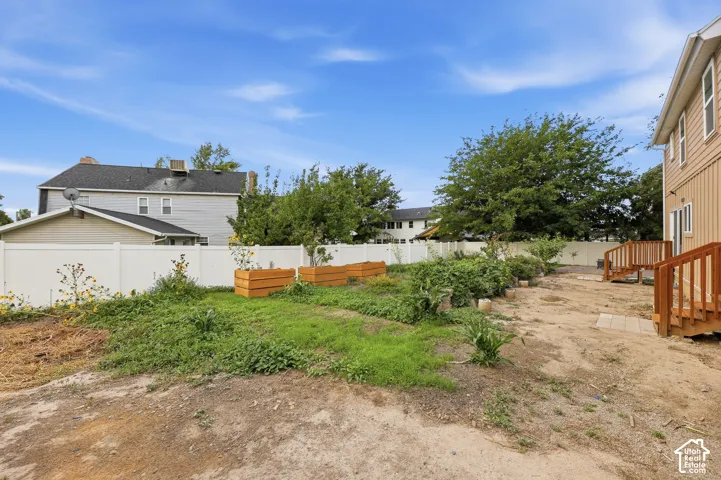 Spacious backyard featuring wood-finish deck access, raised garden beds, and white vinyl perimeter fencing