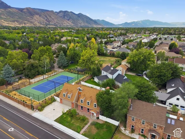Brick exterior with dormer windows, attached garage, concrete driveway, and adjacent tennis court with fencing