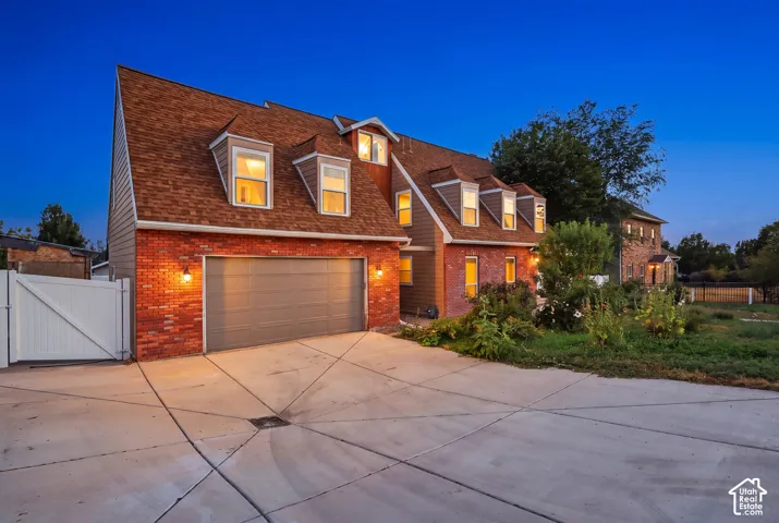 Brick facade with siding accents, attached garage, multiple dormer windows, and a paved driveway