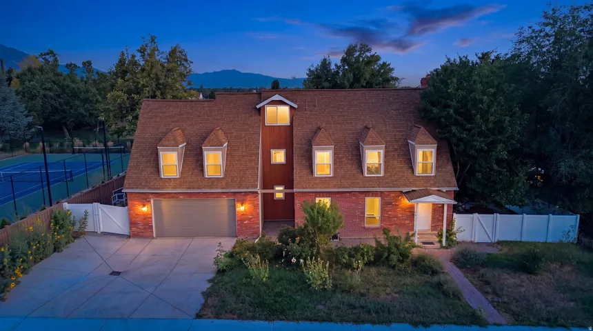 Brick facade, dormer windows, attached garage, concrete driveway, and a private tennis court