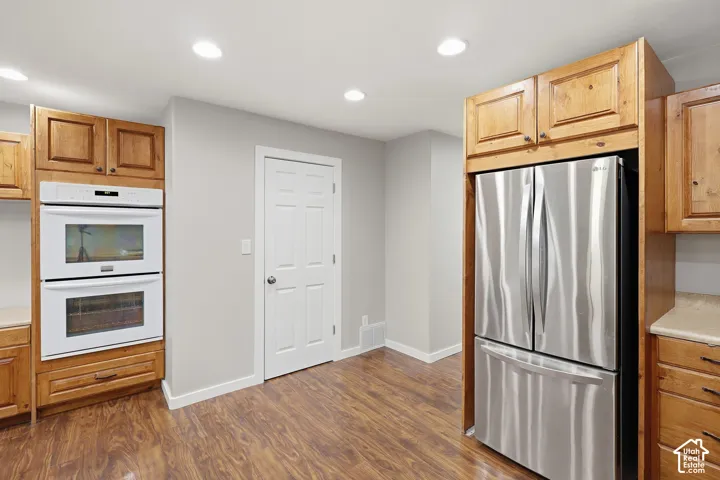 Stainless steel refrigerator, built-in double ovens, wood-finish cabinetry, recessed ceiling lighting, and wood-finish flooring