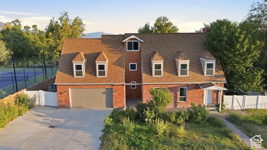 Brick exterior with dormer windows, attached garage, covered entry, and a dedicated tennis court
