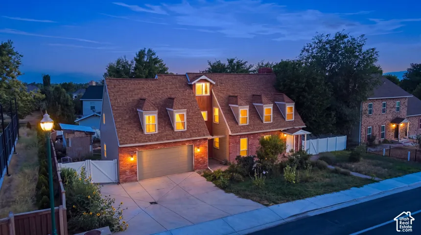 Brick exterior with dormer windows, attached garage, concrete driveway, and white fencing