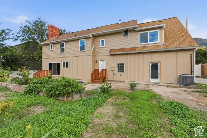 Rear elevation with tan siding, red brick chimney, and a wooden deck with railing
