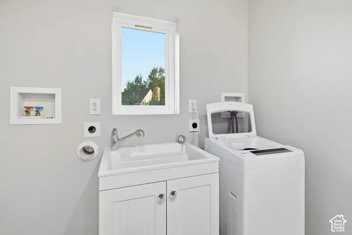 White utility sink with integrated faucet, white base cabinet with crystal knobs, and a white framed window