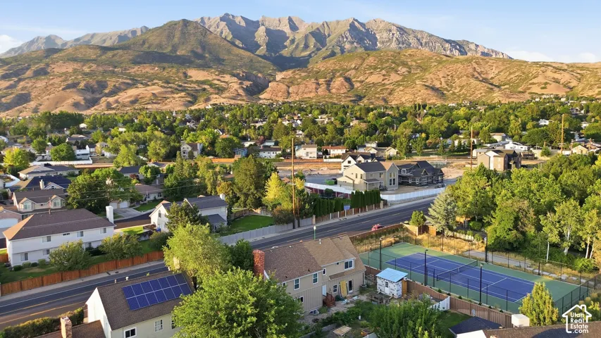 Expansive mountain range backdrop, mature trees, residential neighborhood setting, multi-lane roadway, and a tennis court with fencing