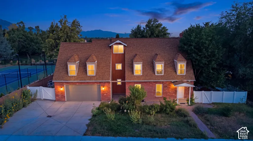 Brick facade, dormer windows, attached garage, concrete driveway, and a private tennis court