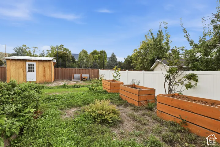 Fenced backyard with a wood-sided shed, multiple large raised garden beds, and a white privacy fence