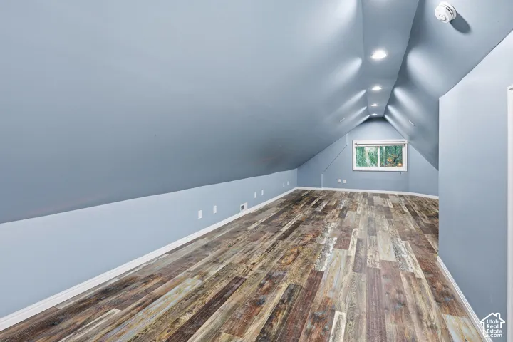 Vaulted ceiling with recessed lighting, wood-finish flooring, and a window providing natural illumination