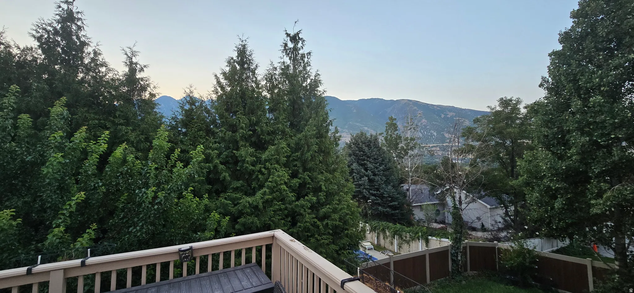 Expansive outdoor deck with a wooden railing, surrounded by mature trees and offering a mountain backdrop