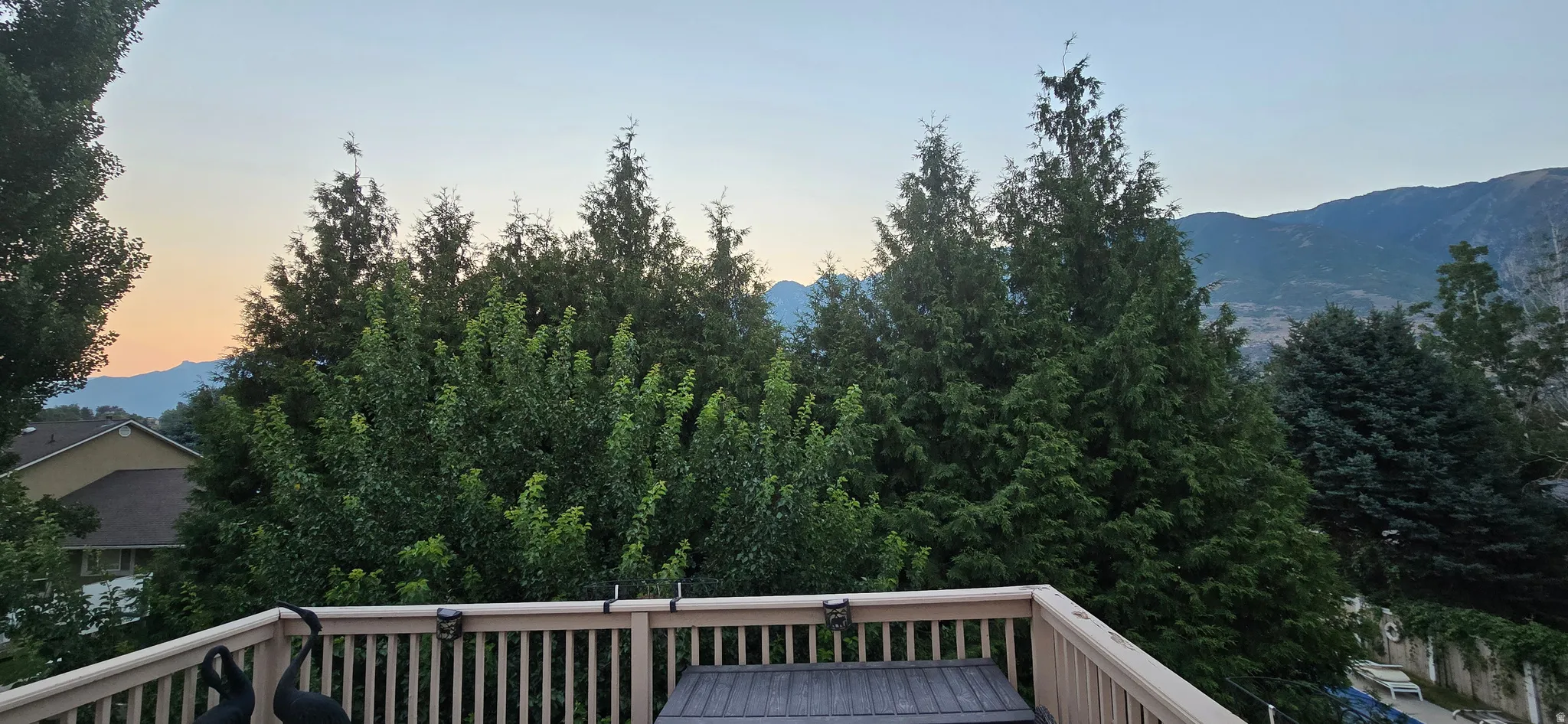 Wood-finish deck with vertical spindle railing, framed by mature trees and distant mountains