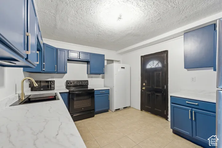 Kitchen featuring blue shaker-style cabinetry, white countertops, stainless steel sink, and a gold-finish faucet