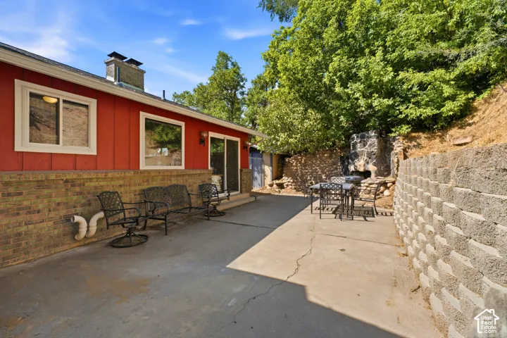 Concrete patio with a retaining wall, a built-in stone fireplace, and a red siding exterior with brick wainscoting