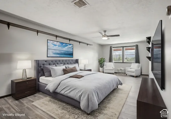 Light wood-finish flooring, ceiling fan with integrated lighting, built-in shelving, dual windows, and light gray wall paint