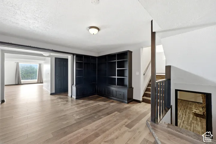 Wood-finish flooring, built-in shelving, staircase with dark wood newel posts and railings, and a wide entryway