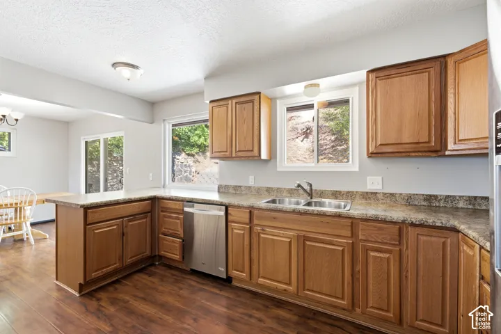 Kitchen featuring wood-finish flooring, wood cabinetry, stone-finish countertops, stainless steel dishwasher, and a double basin sink