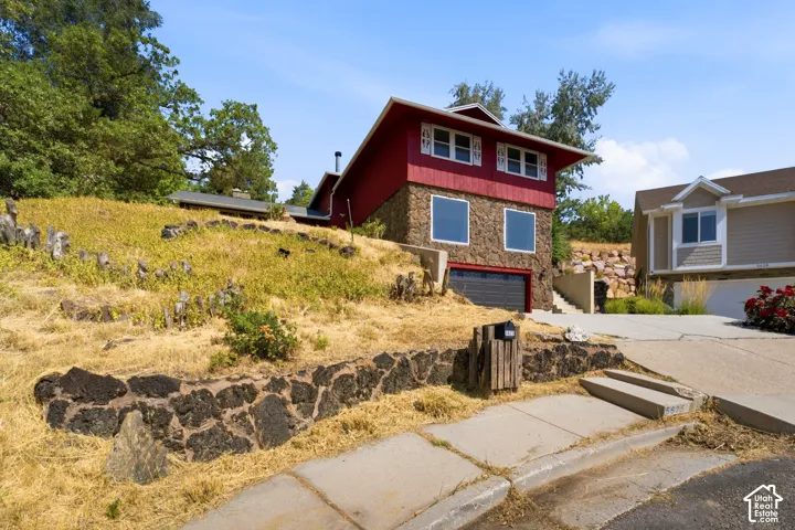 Multi-level exterior with a red siding and stone facade, featuring an integrated garage, multiple windows, and a stone retaining wall
