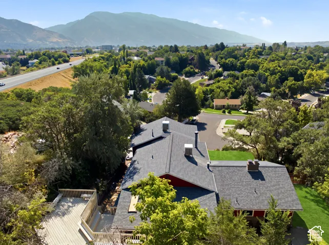 Expansive property featuring a multi-level deck, mature trees, mountain backdrop, and a highway