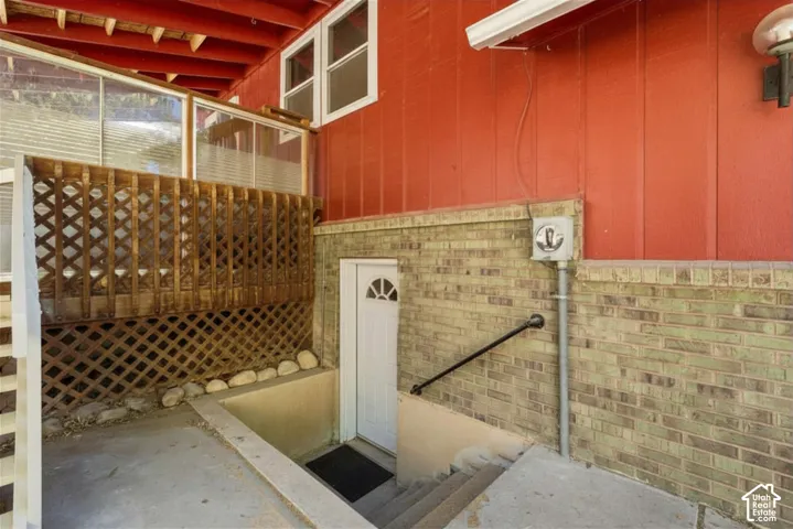 Exterior entry with brick siding, a white entry door, and a black handrail descending concrete steps