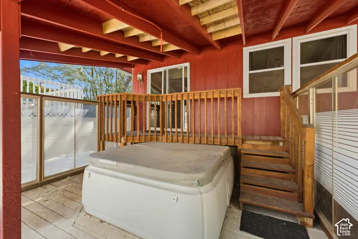 Covered outdoor patio with a spa, wood-finish railing, and exposed ceiling beams