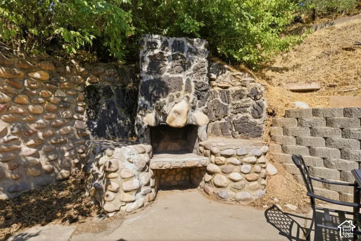 Stone-clad outdoor fireplace with hearth, integrated stone seating, and a concrete patio surface