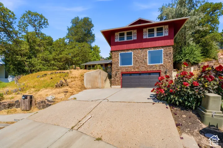 Stone veneer exterior with a red-clad upper level, prominent windows, and an attached garage
