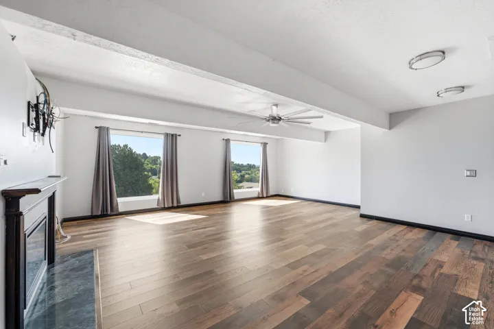 Spacious room featuring wood-finish flooring, a built-in fireplace with a dark mantel and stone hearth, multiple windows, a ceiling fan, and recessed lighting