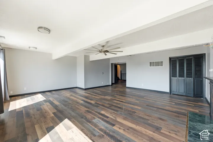 Spacious room with wood-finish flooring, light grey walls, ceiling fan with integrated lighting, and dark louvered closet doors