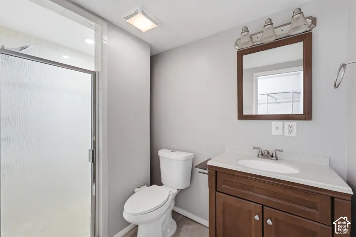 Shower with frosted glass enclosure, single vanity with wood-finish cabinetry, light-toned countertop, and mirror with wood-finish frame