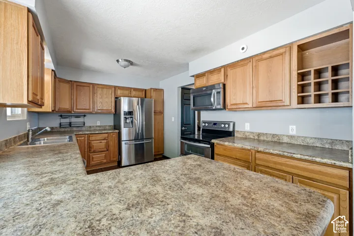 Spacious kitchen featuring wood cabinetry, granite countertops, stainless steel appliances including a refrigerator and range, and ample counter space anchored by a large island