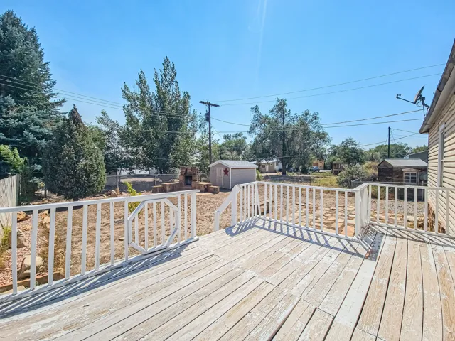 Expansive deck with white railings, leading to a yard featuring a stone fire pit, a small shed, and mature trees