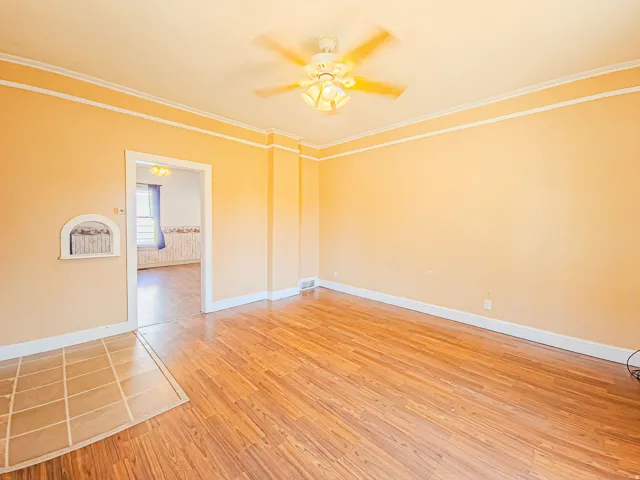 View into kitchen, wood-finish flooring, ceiling fan with integrated lighting, wall niche, and crown molding