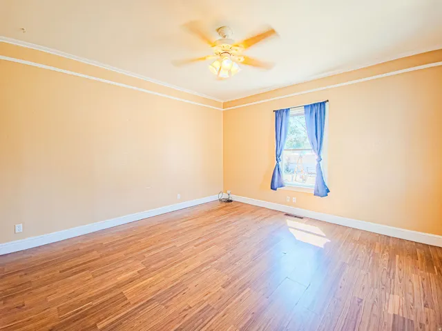 Wood-finish flooring, ceiling fan, crown molding, and window with natural light