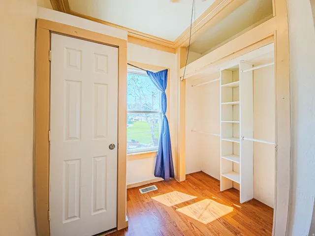 Wood-finish flooring, built-in shelving, paneled interior door, and window with natural light