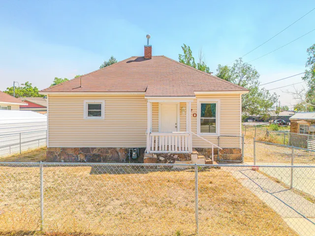 Yellow siding exterior with a pitched roof, stone foundation, covered front porch, and a chain-link fence