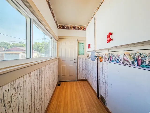 Laundry/Mud Room Wood-finish flooring, white paneled wall treatment, white upper cabinetry, and a white rear entry door
